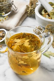 Freshly brewed tea and dried herbs on white marble table