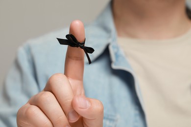 Man showing index finger with tied bow as reminder against light grey background, focus on hand