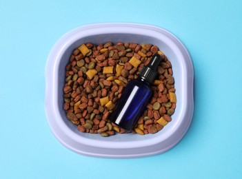 Glass bottle of tincture and dry pet food in bowl on light blue background, top view