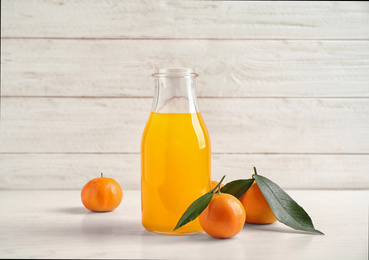 Fresh tangerines and bottle of juice on white wooden table