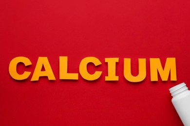 Photo of Word Calcium made of orange letters and open bottle on red background, flat lay