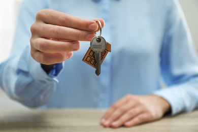 Real estate agent holding house key with trinket at wooden table, closeup