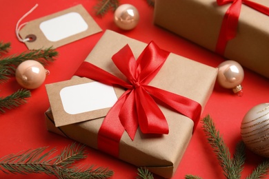 Gift box with blank tag and Christmas decor on red background, closeup