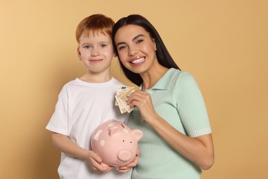 Mother and her son with ceramic piggy bank on beige background