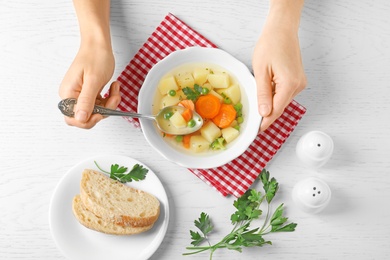 Woman eating fresh homemade vegetable soup at white wooden table, top view