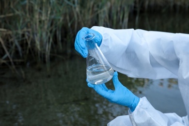Scientist with conical flask taking sample from river for analysis, closeup