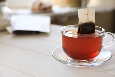 Taking tea bag out of cup at white wooden table indoors, closeup. Space for text