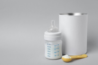 Blank can of powdered infant formula with scoop and feeding bottle on light grey background, space for text. Baby milk