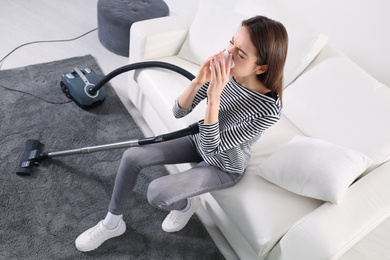 Young woman suffering from dust allergy while vacuuming house