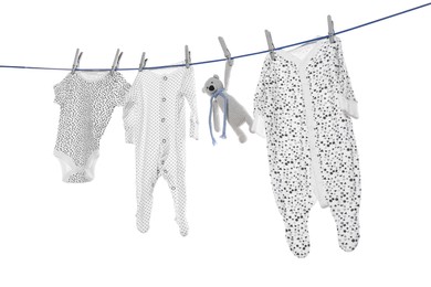 Different baby clothes and toy drying on laundry line against white background