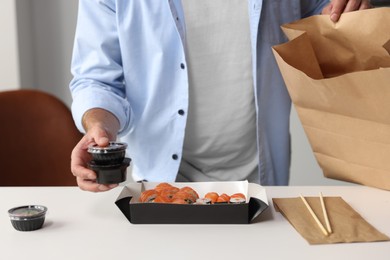 Photo of Man unpacking his order from sushi restaurant at table in room, closeup