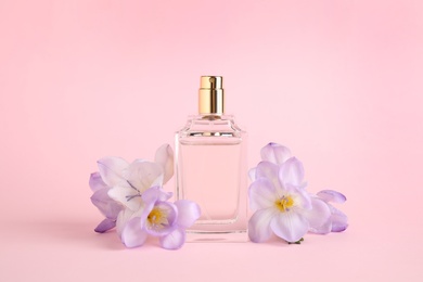 Photo of Bottle of perfume with freesia flowers on pink background