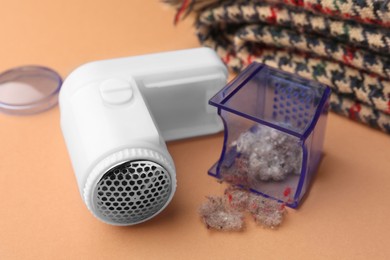Photo of Modern fabric shaver with fuzz and scarf on pale orange background, closeup