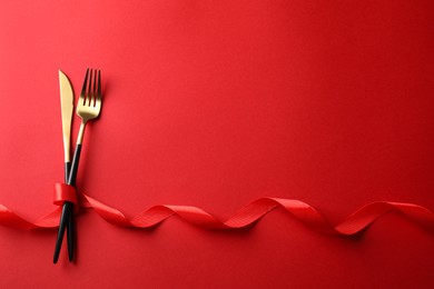 Photo of Cutlery set and ribbon on red background, flat lay with space for text. Romantic table setting