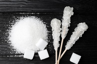 Different types of sugar on black wooden table, flat lay