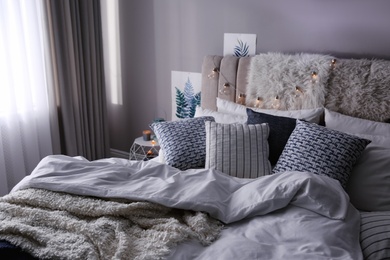 Photo of Bed with warm blanket and cushions in room. Interior design