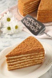 Slice of delicious layered honey cake served on white marble table, closeup
