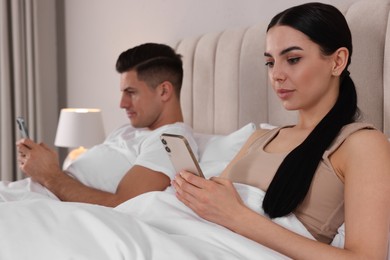Internet addiction. Couple with smartphones in bed indoors