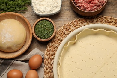 Photo of Flat lay composition with raw dough and ingredients on wooden table. Baking meat pie