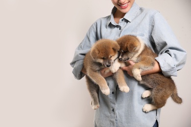 Photo of Woman holding Akita Inu puppies on light background, closeup. Space for text