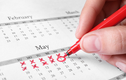 Woman marking date in calendar with red felt pen, closeup