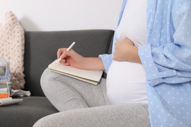 Pregnant woman preparing list of necessary items to bring into maternity hospital at home, closeup