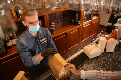Waiter giving packed takeout order to customer in restaurant. Food service during coronavirus quarantine