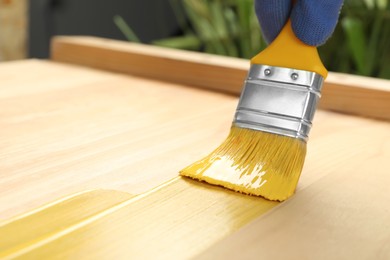 Worker applying yellow paint onto wooden surface, closeup. Space for text