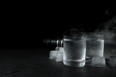 Vodka in shot glasses with ice on table against black background, space for text