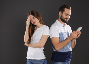 Man with smartphone ignoring his girlfriend on black background. Relationship problems