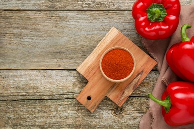 Photo of Bowl with aromatic paprika powder and fresh bell peppers on old wooden table, flat lay. Space for text