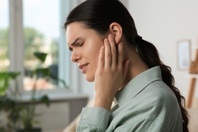 Photo of Young woman suffering from ear pain in room