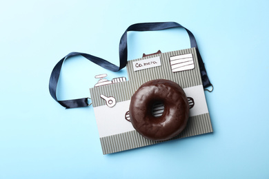 Camera made from donut and piece of cardboard on light blue background, top view