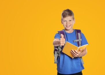 Image of Cute boy with school stationery showing thumbs up on yellow background, space for text
