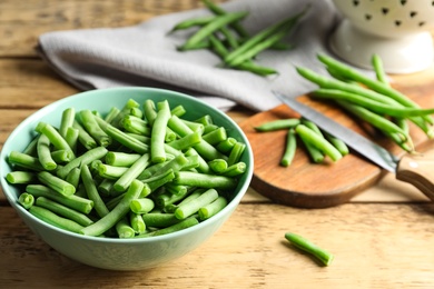 Fresh green beans in bowl on wooden table, closeup. Space for text