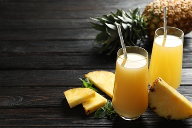 Delicious pineapple juice and fresh fruit on black wooden table. Space for text