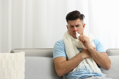 Photo of Ill man using nasal spray on sofa at home