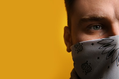 Young man with bandana covering his face on yellow background, closeup. Space for text