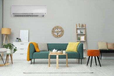 Modern air conditioner on light wall in living room with stylish furniture