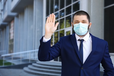 Man in protective face mask showing hello gesture outdoors. Keeping social distance during coronavirus pandemic