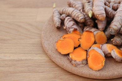 Photo of Board with fresh turmeric roots on wooden table, closeup. Space for text