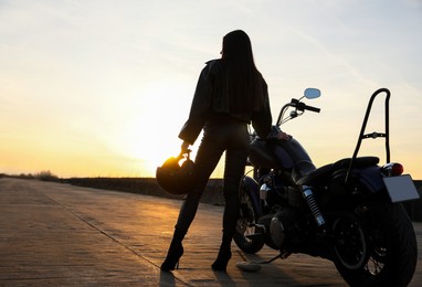 Photo of Woman with helmet near motorcycle at sunset, back view