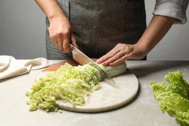 Woman cutting fresh Chinese cabbage at light grey table, closeup