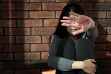 Photo of Domestic violence concept. Woman hiding her face, focus on hand with written word Stop