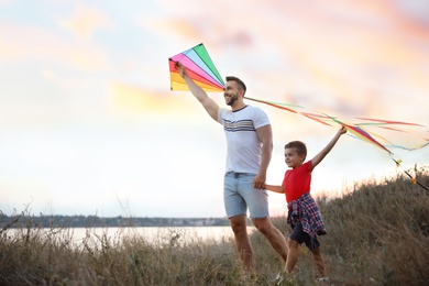 Happy father and his child playing with kites outdoors at sunset. Spending time in nature