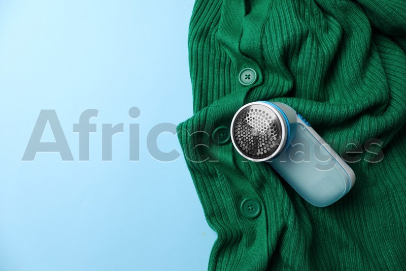 Photo of Modern fabric shaver and woolen cardigan on light blue background, top view. Space for text