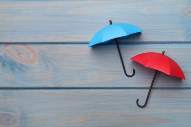 Small color umbrellas on light blue wooden background, flat lay. Space for text