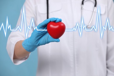 Doctor holding red heart on light blue background, closeup 