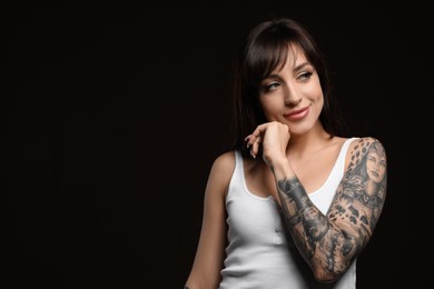 Beautiful woman with tattoos on arm against black background. Space for text