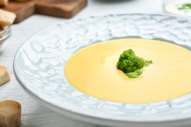 Bowl of cheese cream soup with broccoli served on white wooden table, closeup